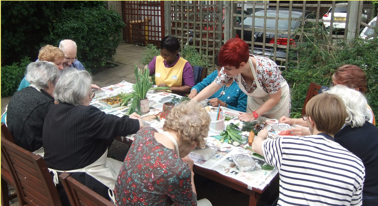 Eine Gruppe von elf PErsonen sitzen um einen Tisch herum und basteln mit Pflanzen