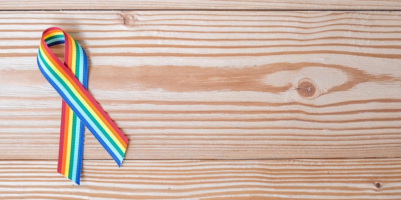 Eine Regenbogen Schleife liegt auf einem Holztisch